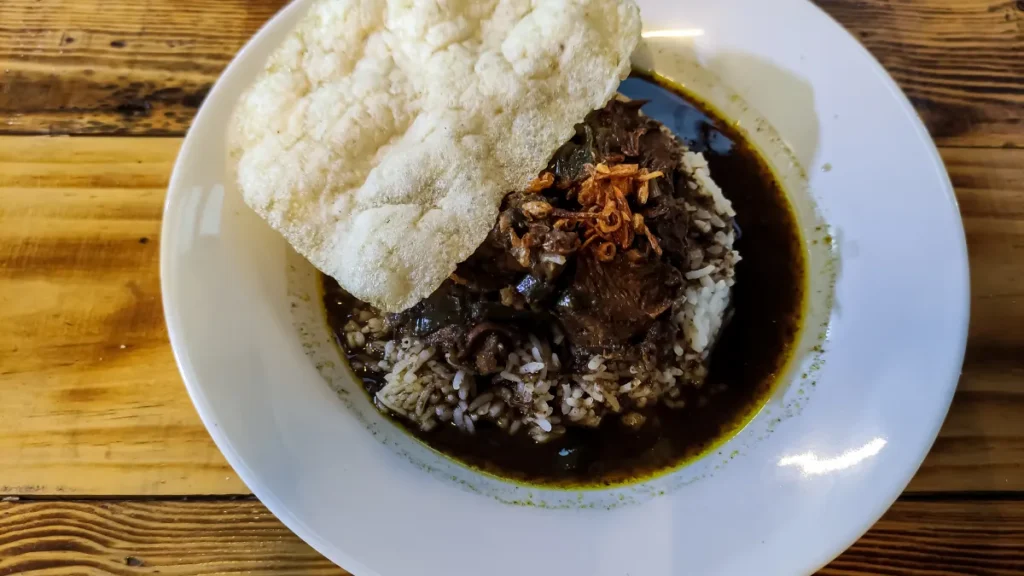 Semangkuk rawon kuah hitam kluwek dengan nasi dan kerupuk udang